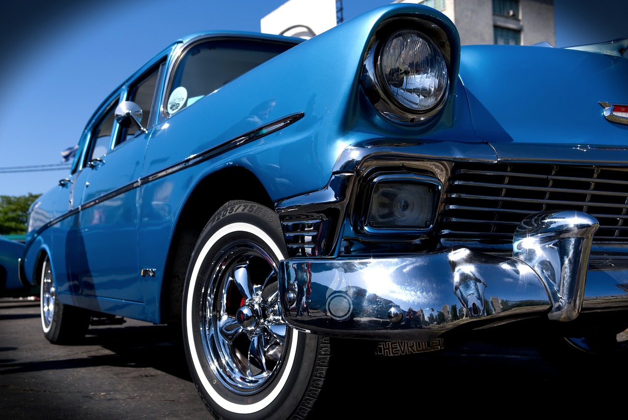 a blue classic car parked in a parking lot, by Dennis Ashbaugh, trending on pixabay, photorealism, chicano airbrush art, zoomed in shots, gleaming silver and rich colors, low wide angle shot