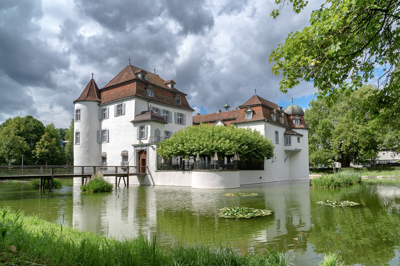 a large white building sitting next to a body of water, by Otto Meyer-Amden, shutterstock, renaissance, moat, garden, malt, adventurer