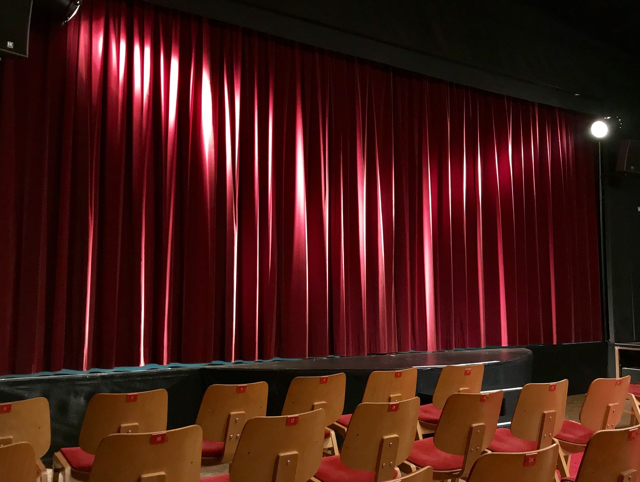 a group of chairs sitting in front of a red curtain, a picture, pexels, backside of scenography elements, college, non-pleated section, shining and happy atmosphere