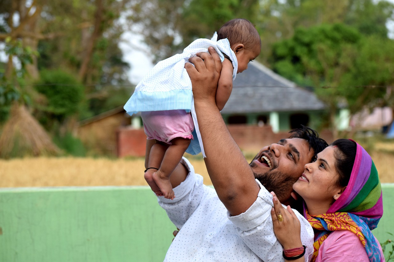 a man holding a baby up in the air, samikshavad, happy family, a long shot, feature, complex background