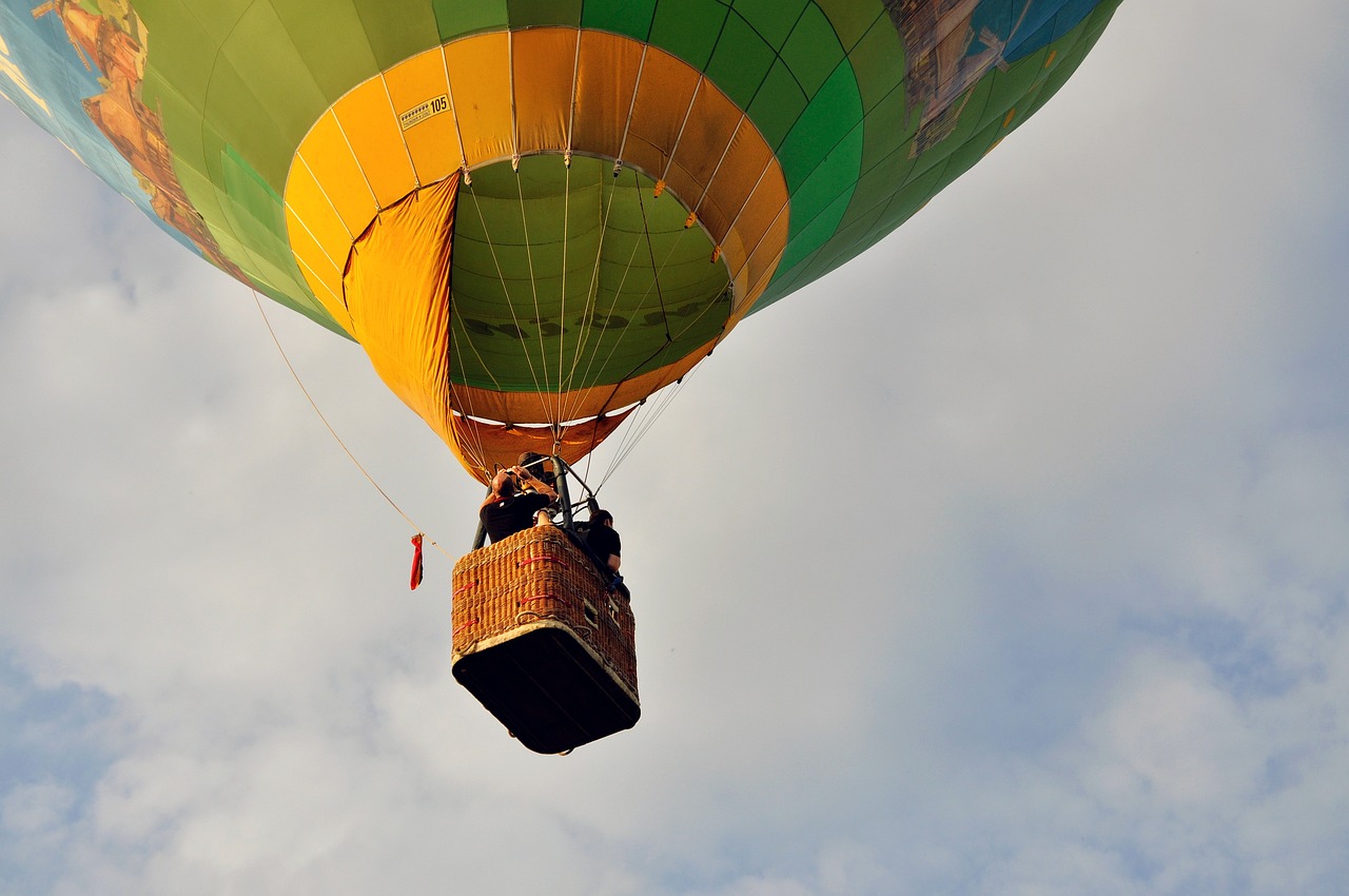 a yellow and green hot air balloon flying in the sky, a picture, by Dave Allsop, pixabay contest winner, figuration libre, with people inside piloting it, slight overcast weather, mid view from below her feet, with a yellow green smog sky