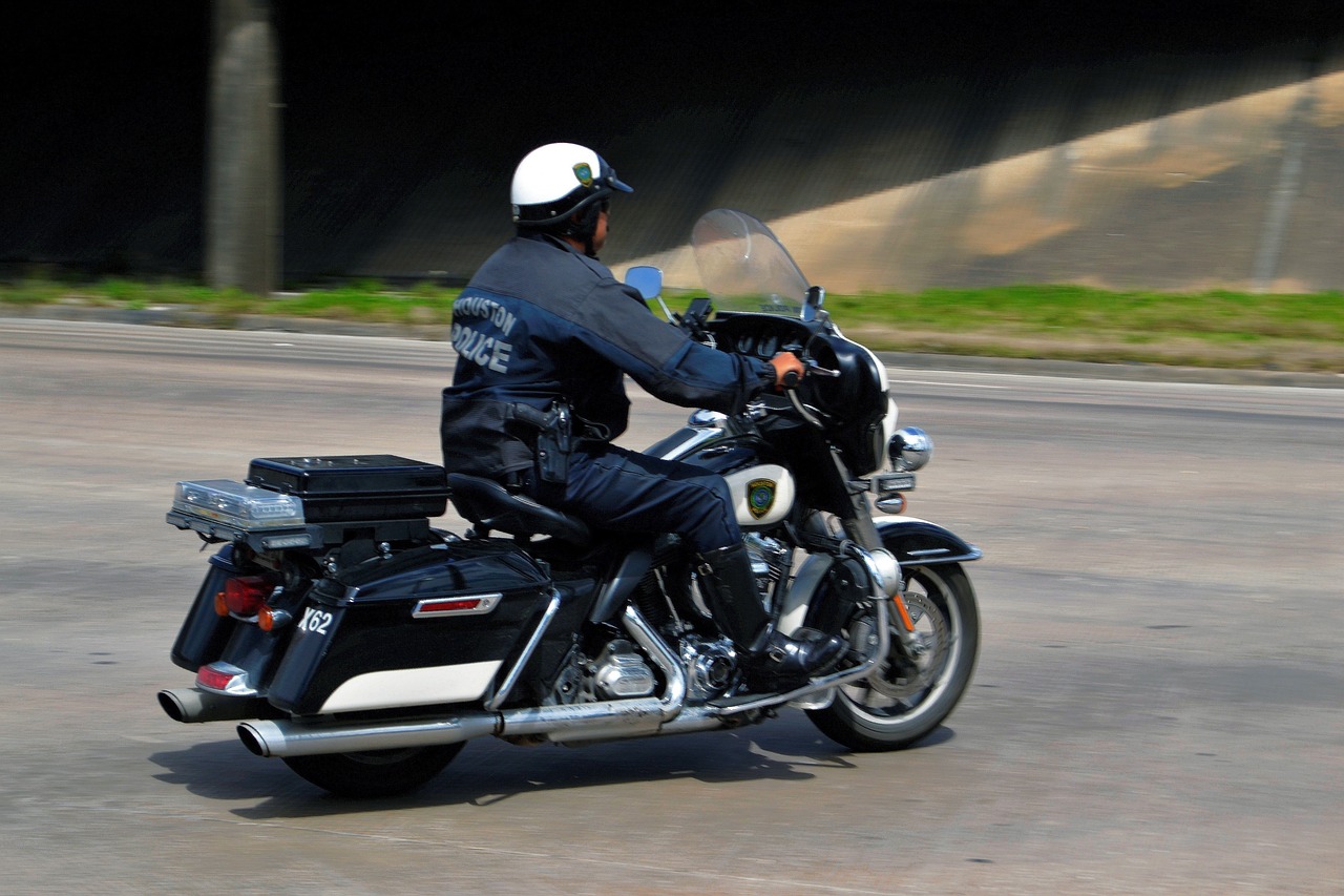 a man riding on the back of a motorcycle down a street, police uniform, tx, visor, from the side