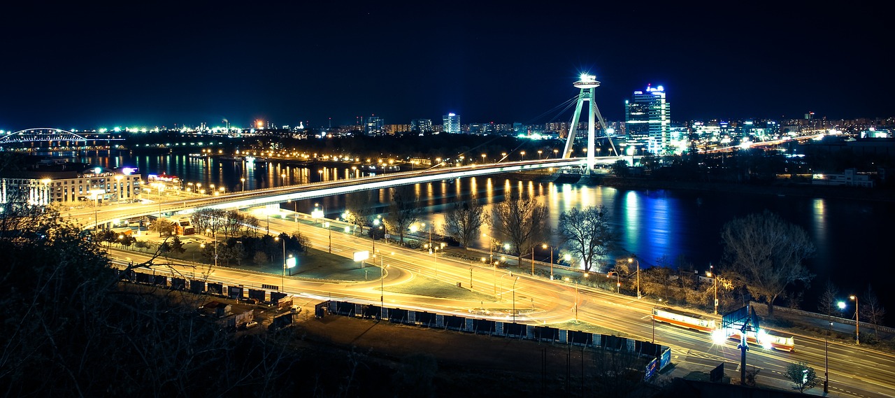 a view of a city at night from the top of a hill, by Antoni Brodowski, shutterstock, 1 glowing bridge crossing river, shot on nikon d 3 2 0 0, riverside, slavic!!!