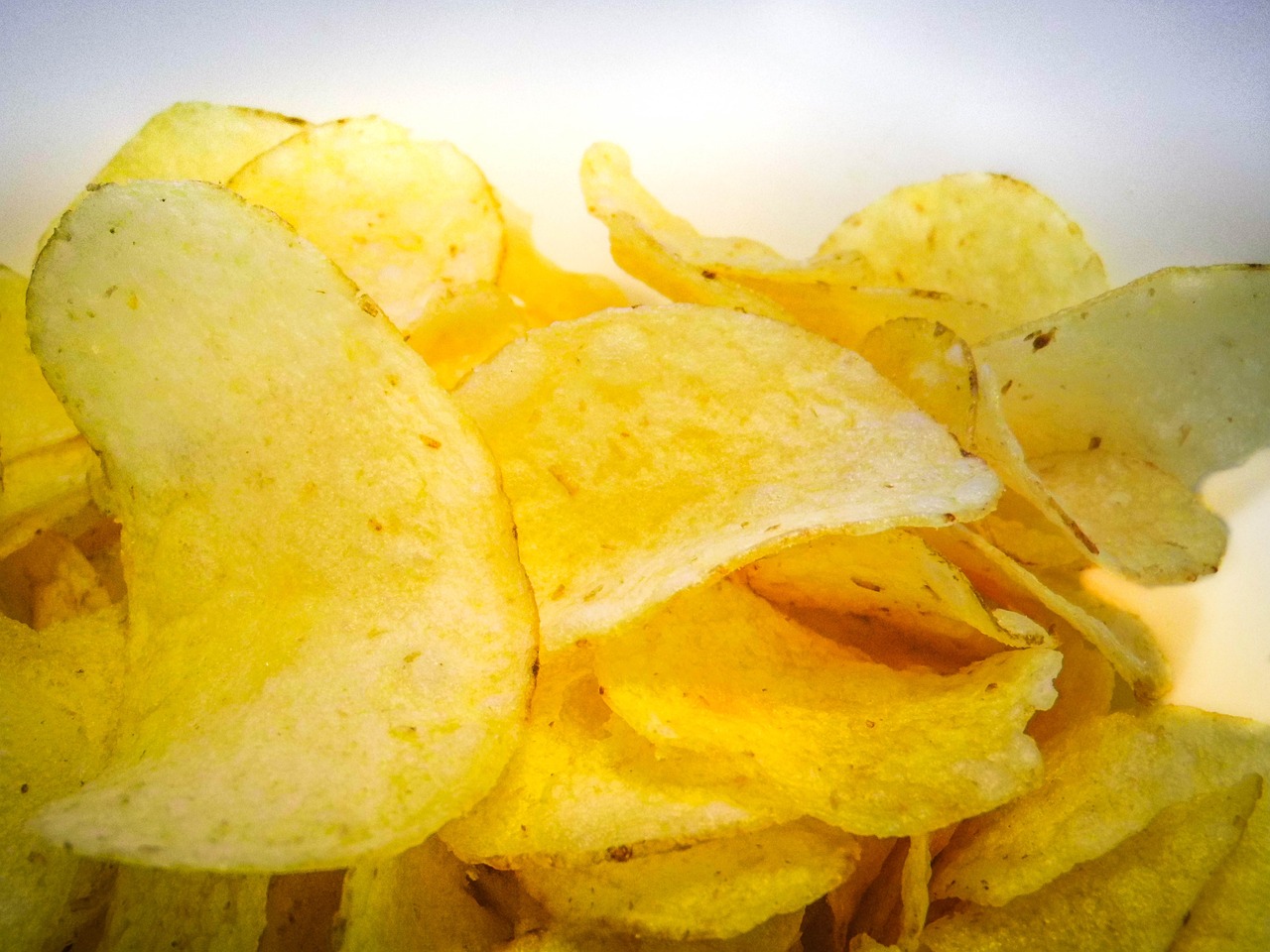 a pile of potato chips sitting on top of a white plate, a picture, pexels, photorealism, shades of yellow, low - angle shot from behind, shaded, innovation