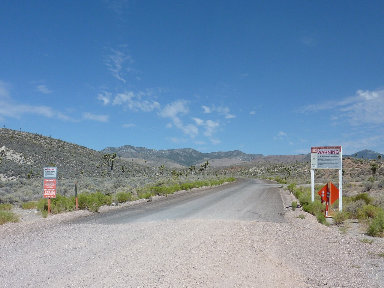 a couple of signs sitting on the side of a road, by Dennis Ashbaugh, les nabis, inside area 51, in the distance is a rocky hill, the gate to hell, year 2 5 0 0