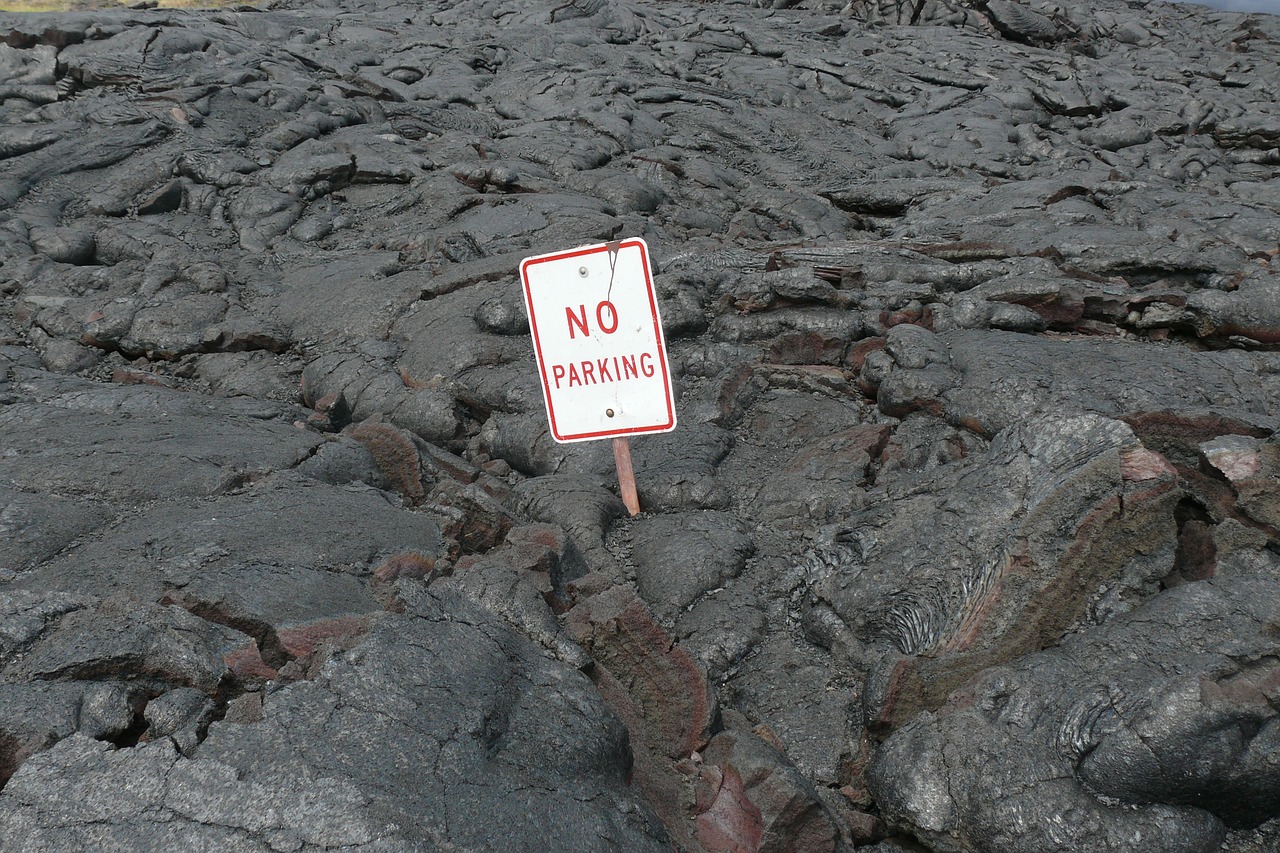a no parking sign sitting on top of a pile of rocks, by Dennis Ashbaugh, flickr, background of a lava river, lava!!!, cracked mud, no flash