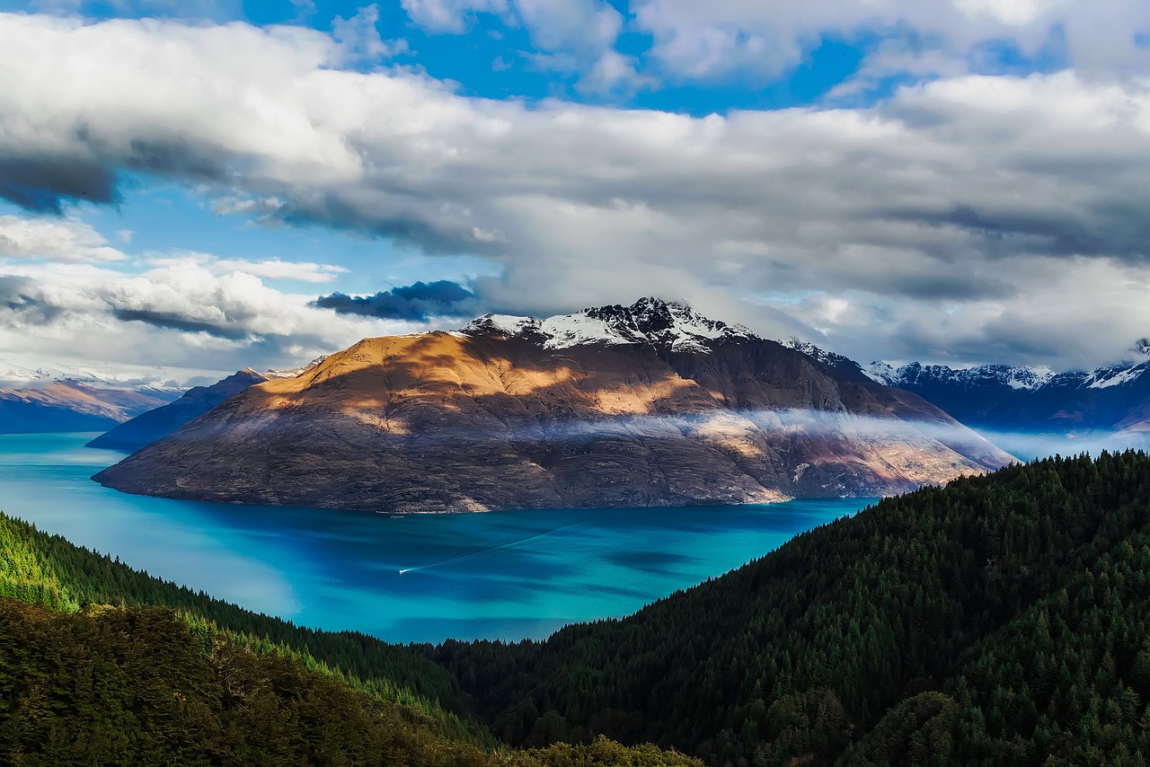 a large body of water surrounded by mountains, a tilt shift photo, by Richard Carline, hurufiyya, new zealand landscape, 4k uhd wallpaper, under blue clouds, ❤🔥🍄🌪