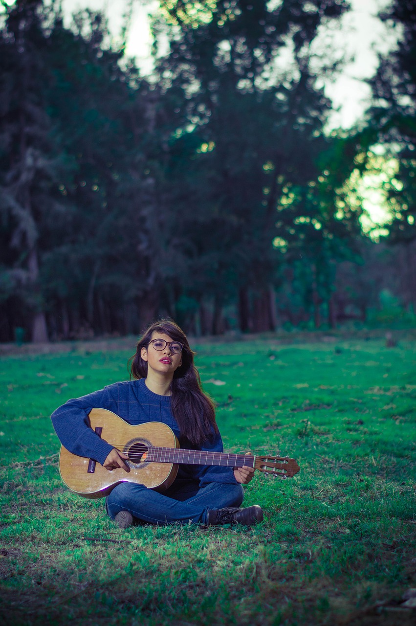 a woman sitting in the grass with a guitar, inspired by Elsa Bleda, in front of a forest background, assamese aesthetic, portrait soft low light, cynthwave