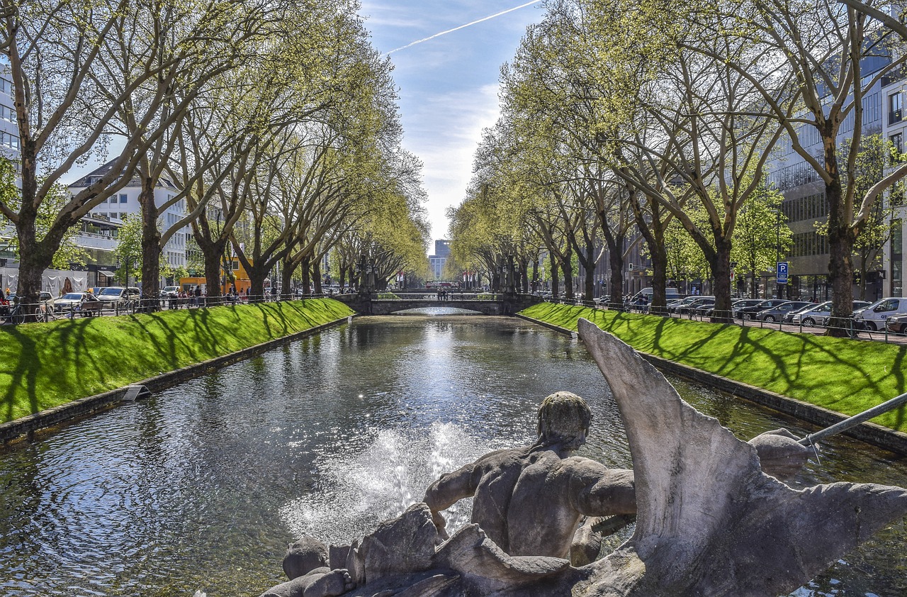 a large body of water surrounded by trees, by david rubín, shutterstock, visual art, city of munich!!!, statue is a fountain, water flowing through the sewer, springtime morning