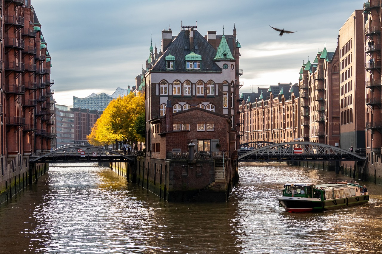 a boat traveling down a river next to tall buildings, a stock photo, by Dirk Helmbreker, timbered house with bricks, river with low flying parrots, during autumn, tourist photo