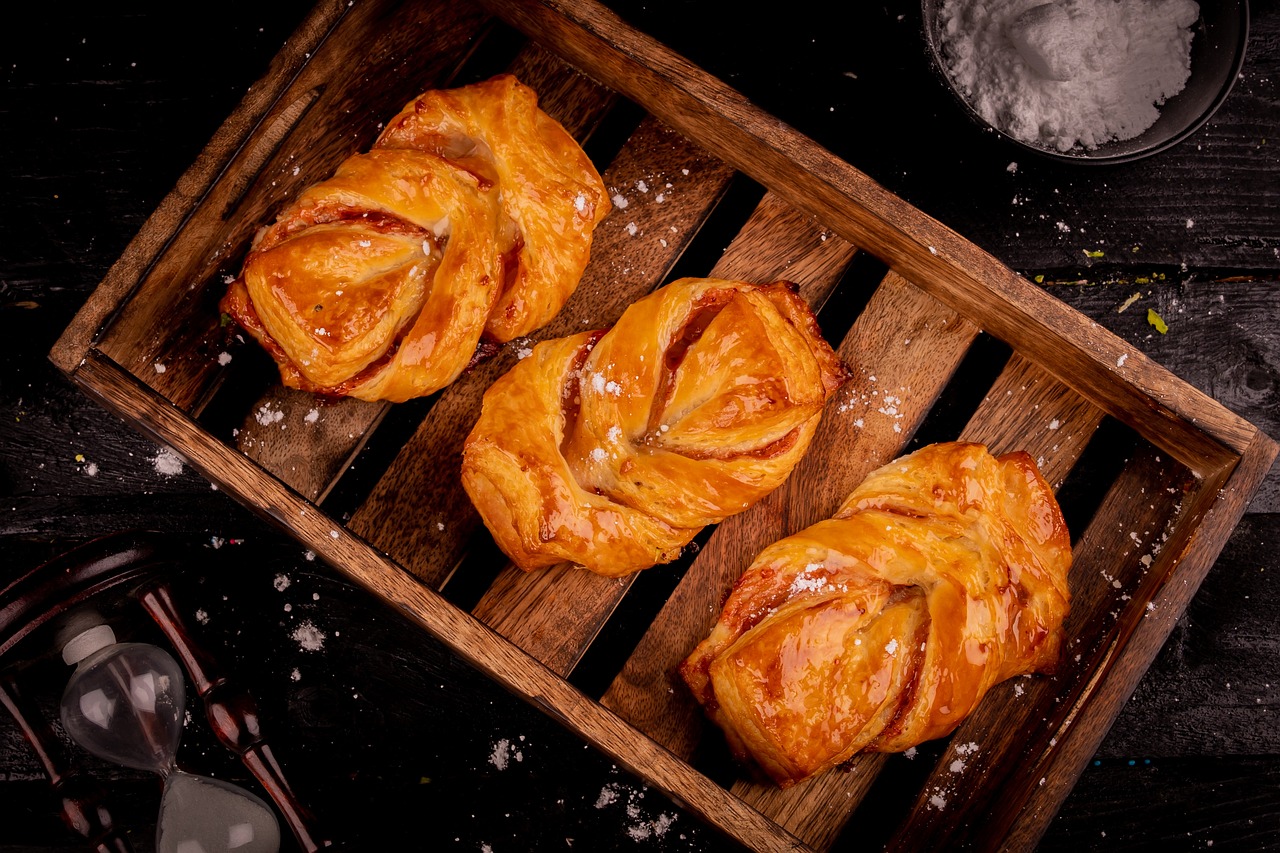 a wooden box filled with pastries sitting on top of a table, inspired by Slava Raškaj, shutterstock, renaissance, on a black background, twisty, crispy buns, high detail product photo