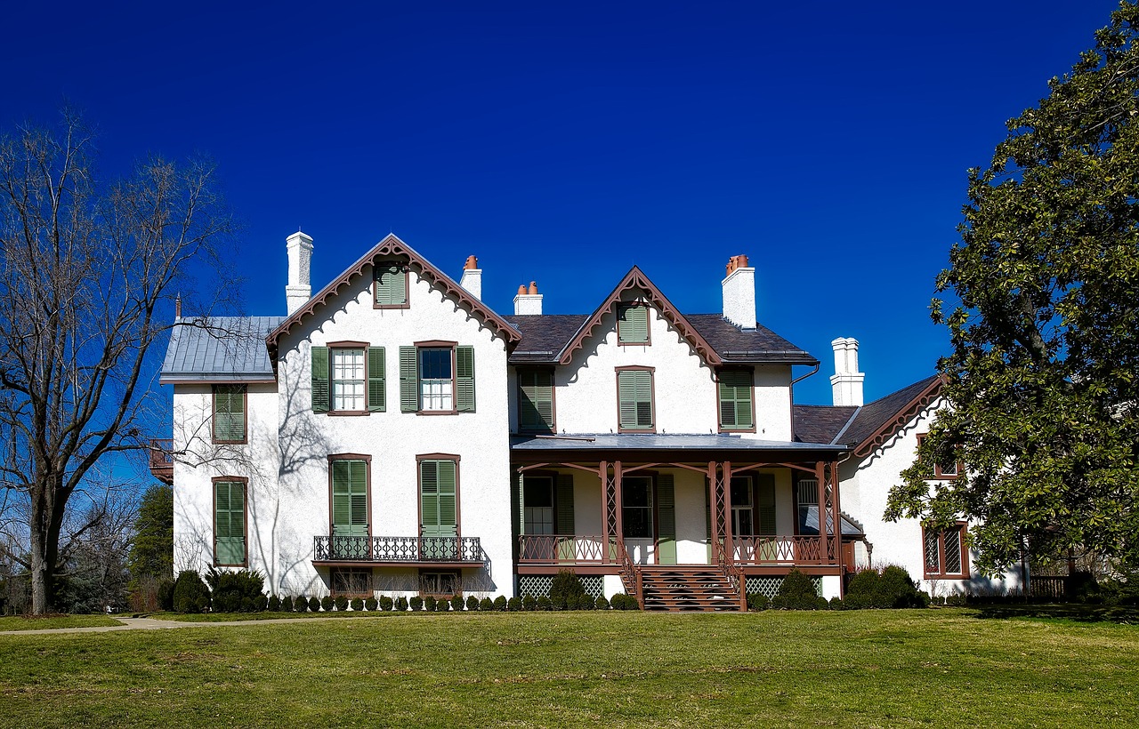 a large white house sitting on top of a lush green field, a portrait, by Randy Post, shutterstock, folk art, edmonia lewis, front elevation view, front and side views, sunlit