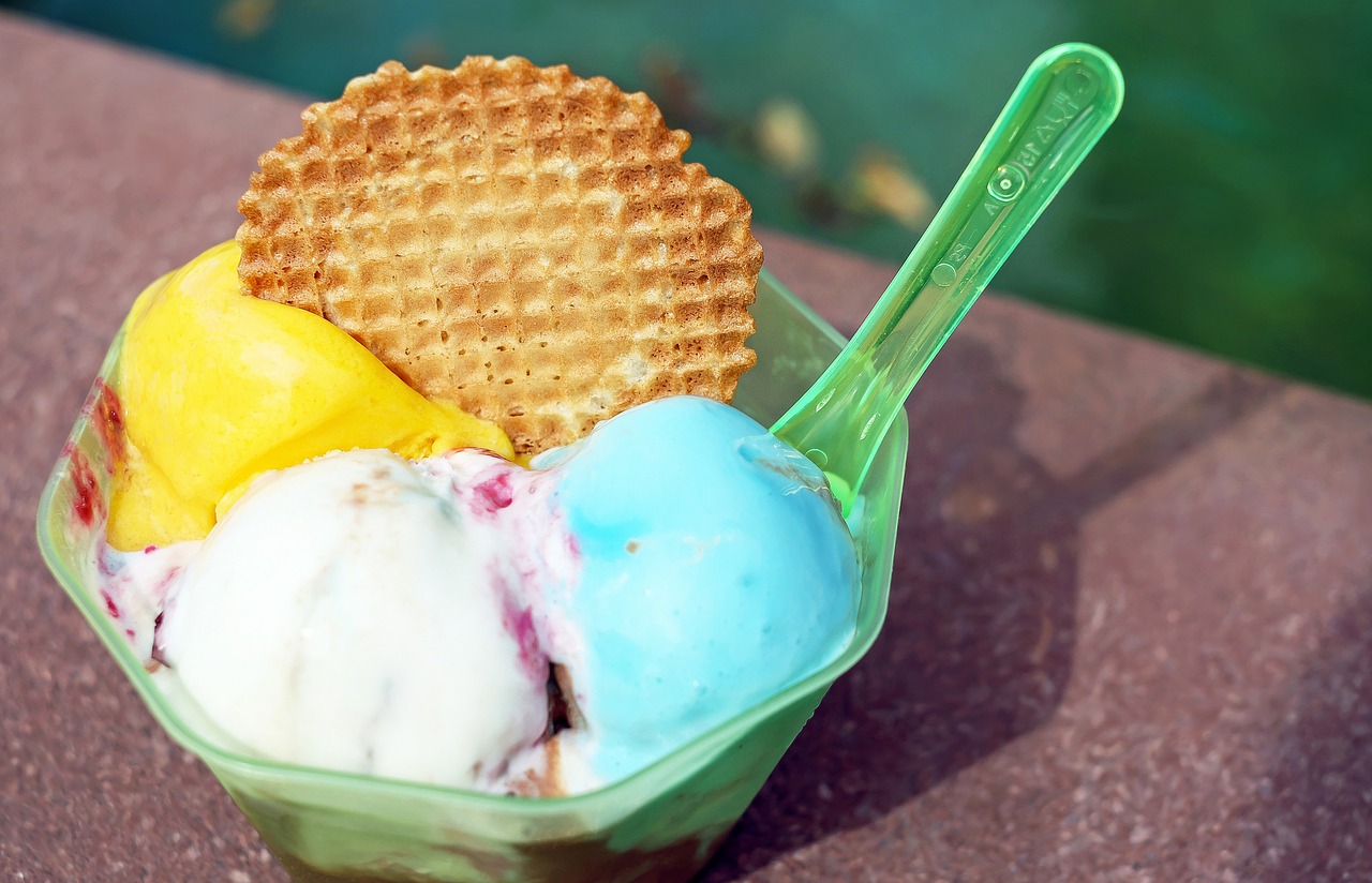 a green container filled with three scoops of ice cream, turquoise pink and yellow, eating outside, blue waffle cone, genesis