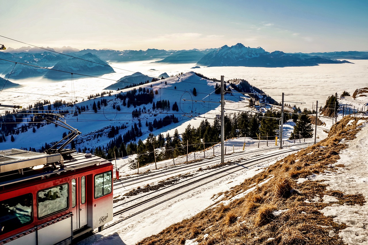 a red and white train traveling down a snow covered slope, by Cedric Peyravernay, shutterstock, view above the clouds, tram, panorama, sunny morning