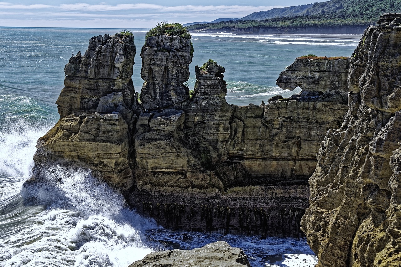 a man standing on top of a cliff next to the ocean, a picture, by Alexander Robertson, shutterstock, chiseled formations, new zealand landscape, crashing waves, tall spires