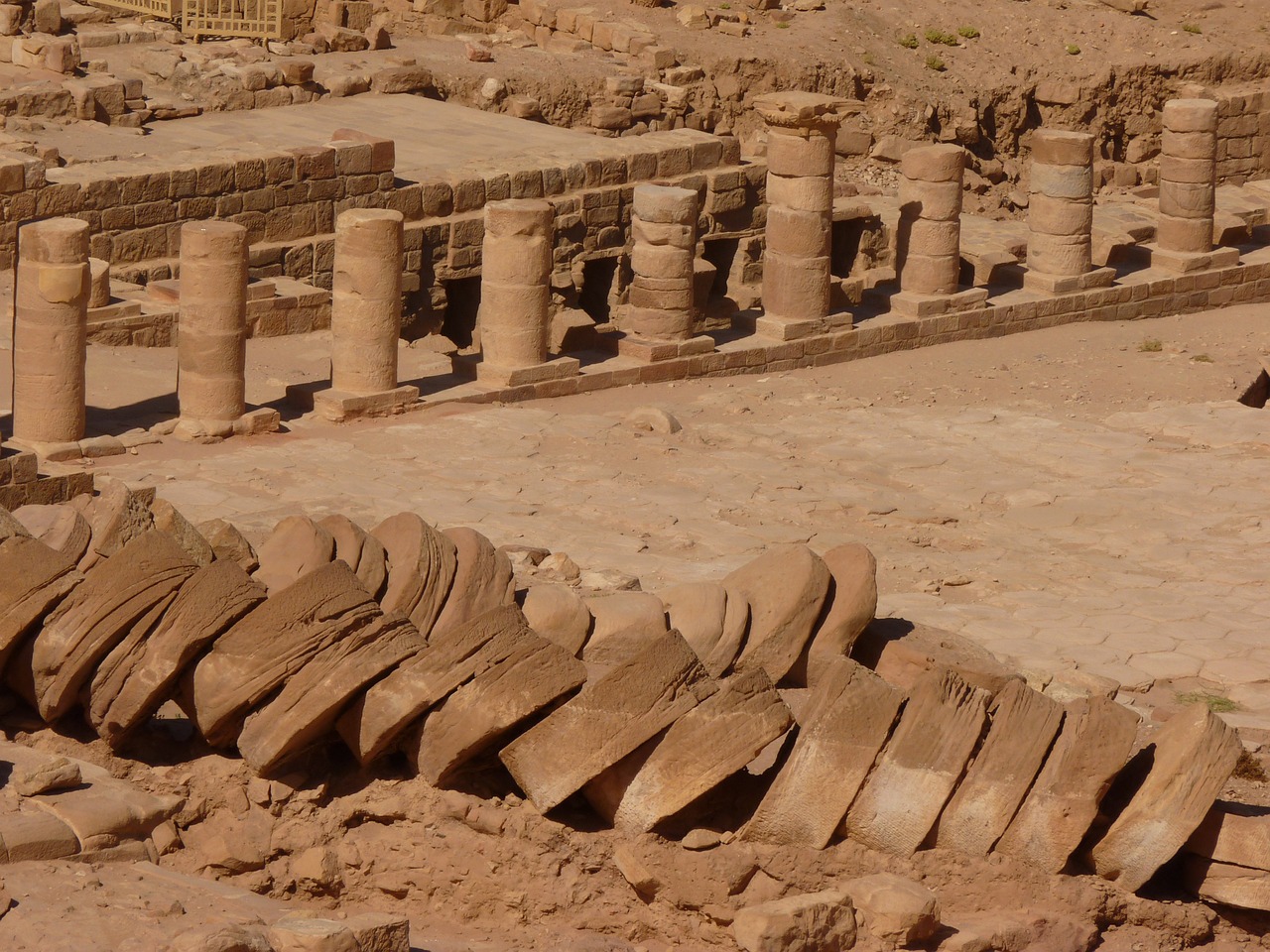 a pile of rocks sitting on top of a dirt field, egyptian art, flickr, roman columns, rows of canteen in background, red sandstone natural sculptures, stepping on towers