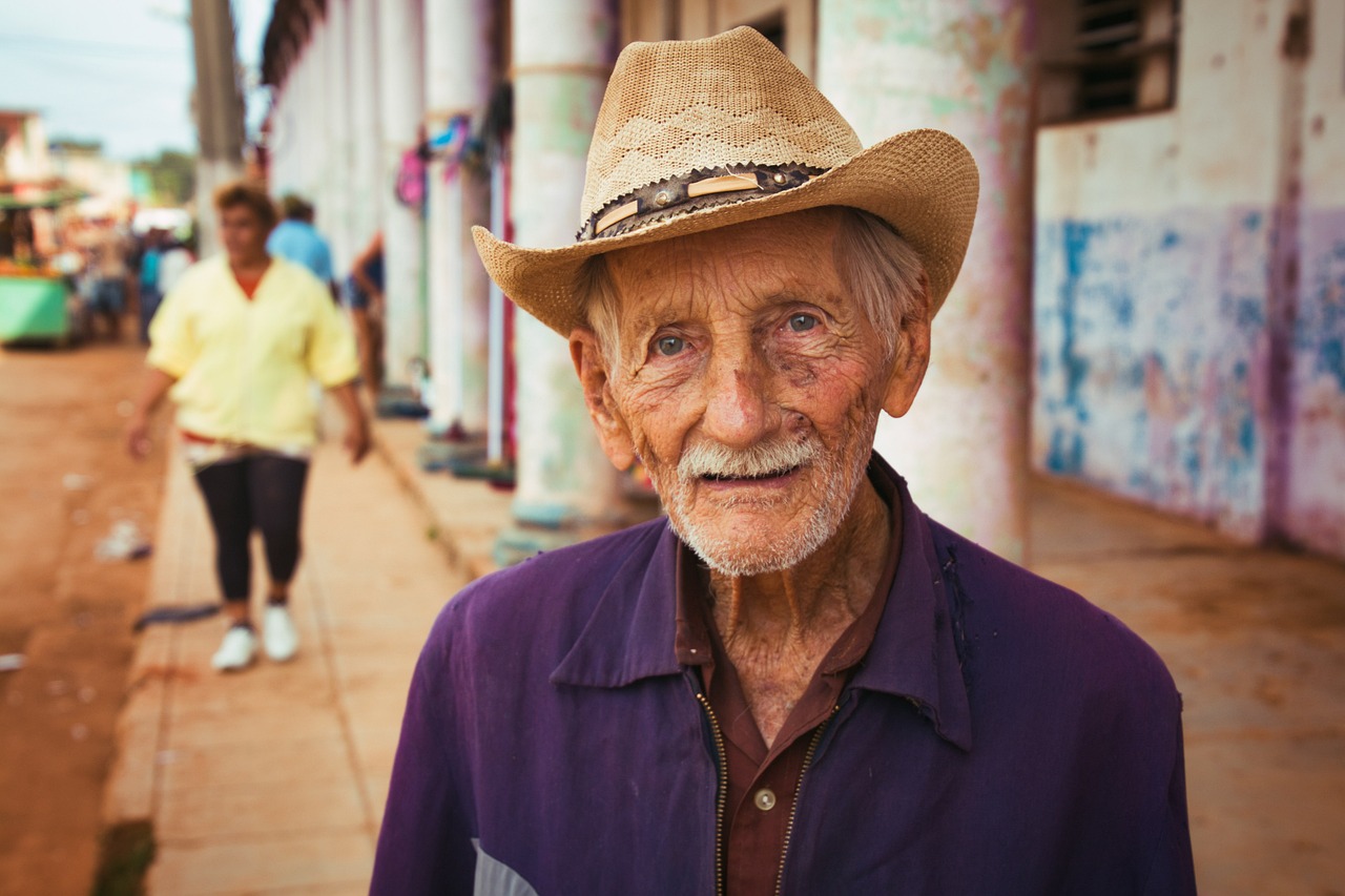 a close up of a person wearing a hat, a portrait, by William Berra, pexels contest winner, cuban setting, old male, square, smiling at camera