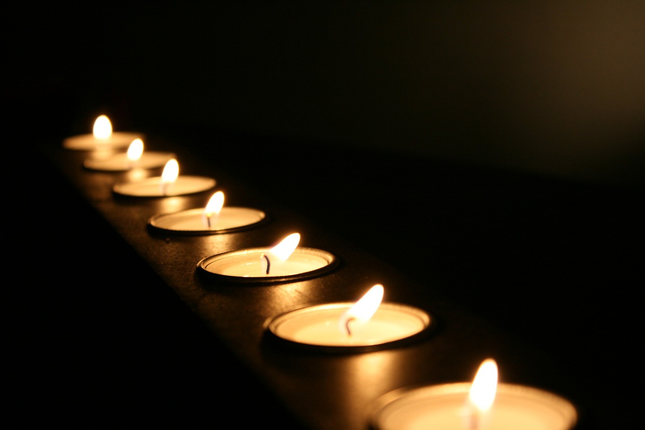 a row of lit candles sitting on top of a table, flickr, dramatic lighting”, volumetric lighting”