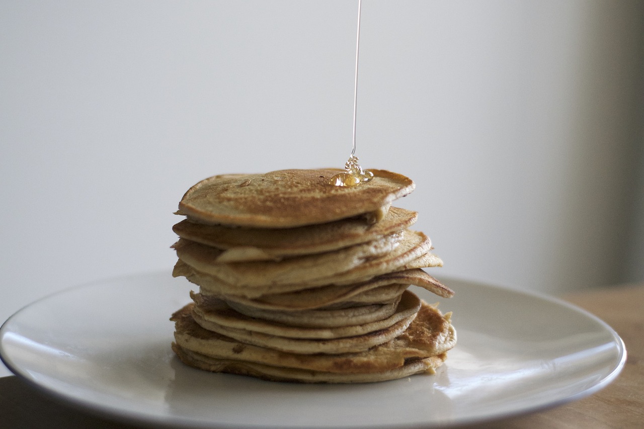 a stack of pancakes being drizzled with syrup, by Alice Mason, unsplash, wikimedia commons, on grey background, natural morning light, filmed in 70mm