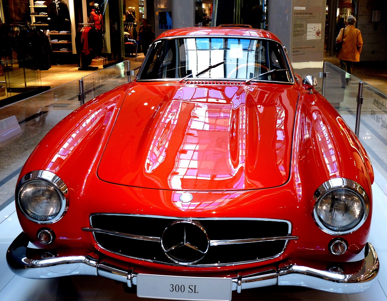 a red car is on display in a museum, a photo, pexels, photorealism, mercedez benz, but very good looking”, shiny skin”, perfect symmetrical image