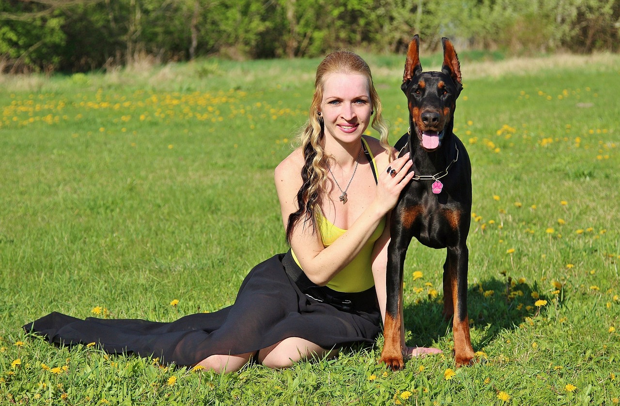 a woman sitting in the grass with a dog, by Eva Švankmajerová, pixabay, she is wearing a black tank top, regal pose, a tall, canines sports photo