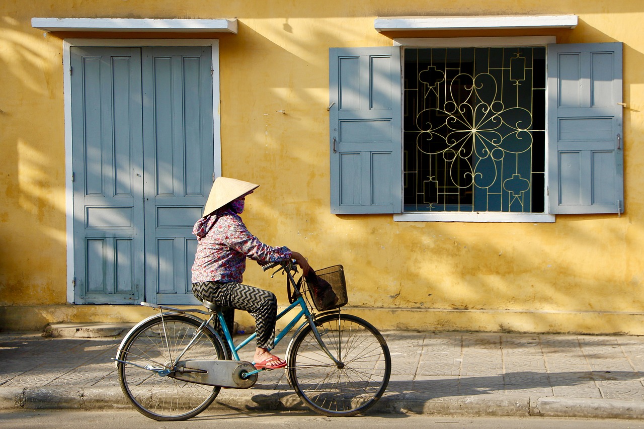 a woman riding a bike in front of a yellow building, flickr, fine art, hue, -640, ap, village