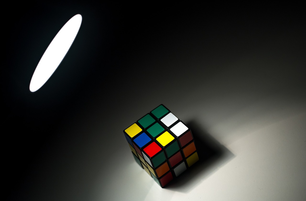 a rubik cube sitting on top of a table, a picture, inspired by Ernő Rubik, cubo-futurism, dark studio light, singular light source from below, light source from the left, studio backlight