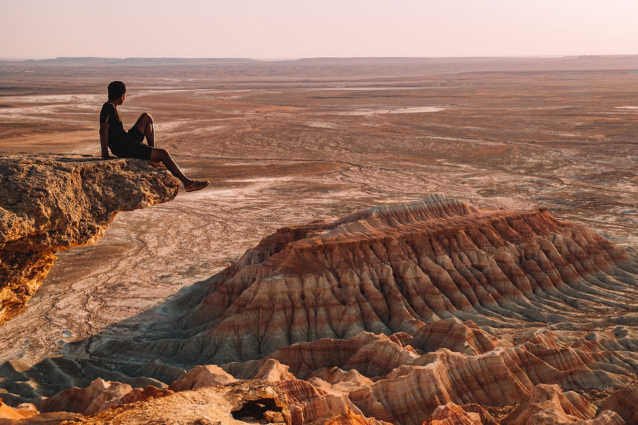 a person sitting on the edge of a cliff, by Andrei Kolkoutine, red desert, ultrawide cinematic, azamat khairov, overlooking