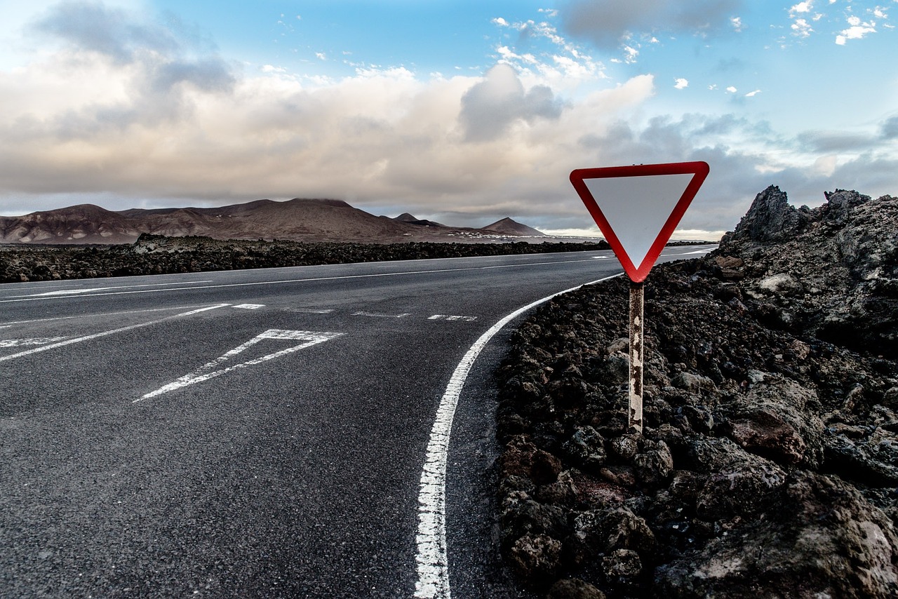 a red triangular sign sitting on the side of a road, a picture, by Niels Lergaard, pexels, lava field, drifting, intersection, slow