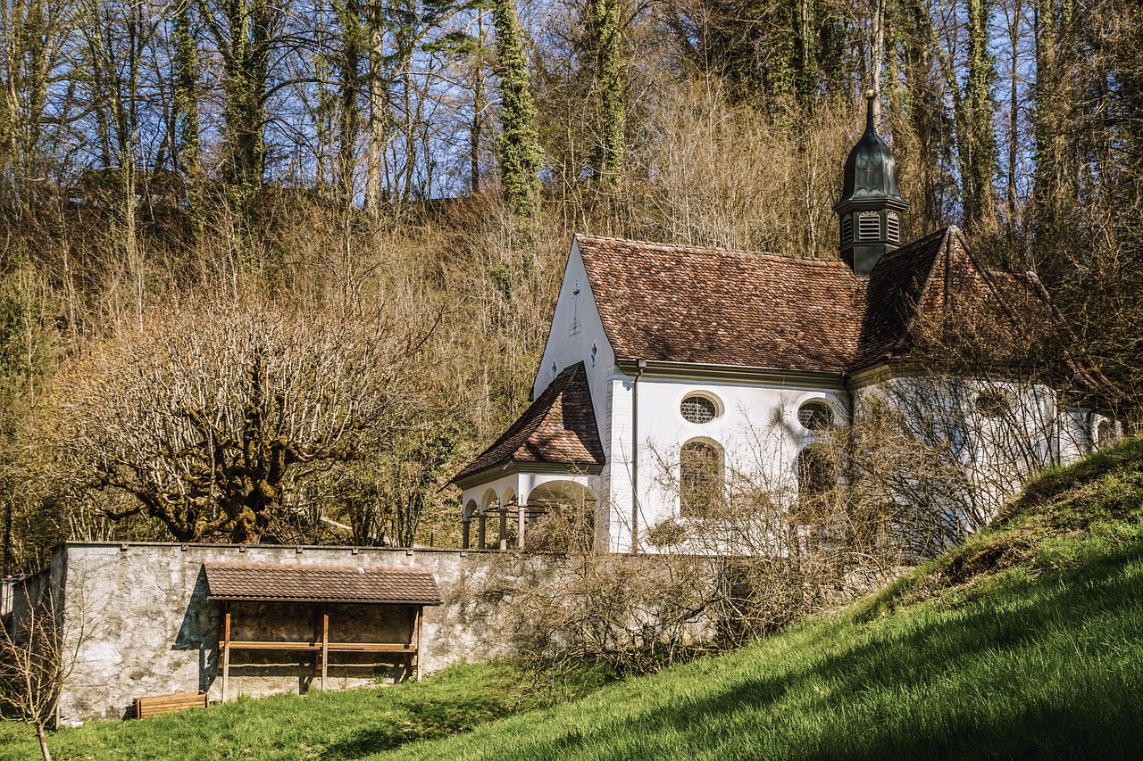 a white building sitting on top of a lush green hillside, a photo, by Otto Meyer-Amden, renaissance, church in the wood, idyllic cottage, february), nice afternoon lighting