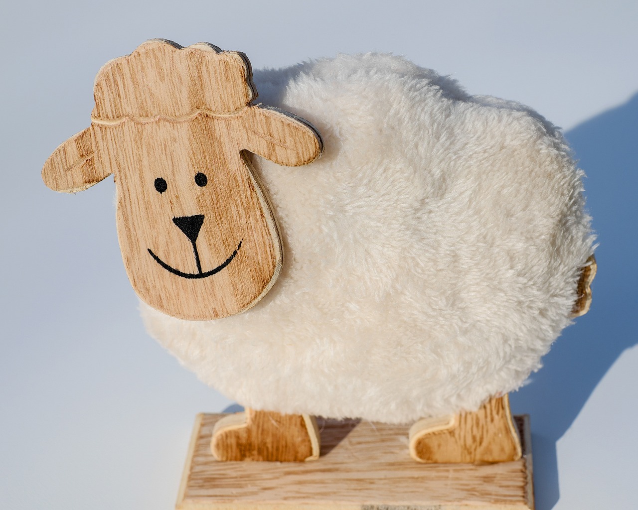 a white sheep sitting on top of a wooden block, inspired by Leo Leuppi, product introduction photo, warm friendly face, folded, fluffy''
