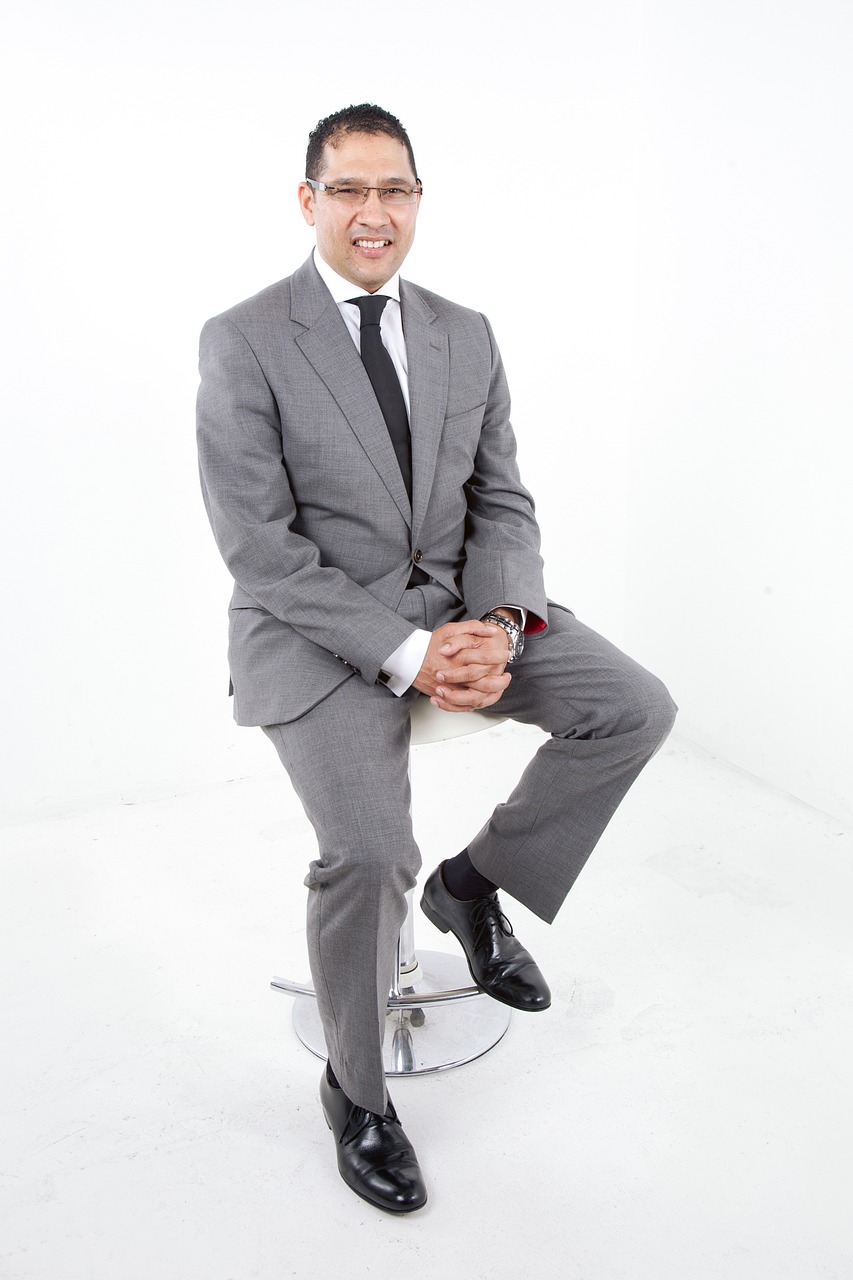 a man in a suit sitting on a stool, by Ric Estrada, elegant smiling pose, kuang hong, 45 years old men, grey suit