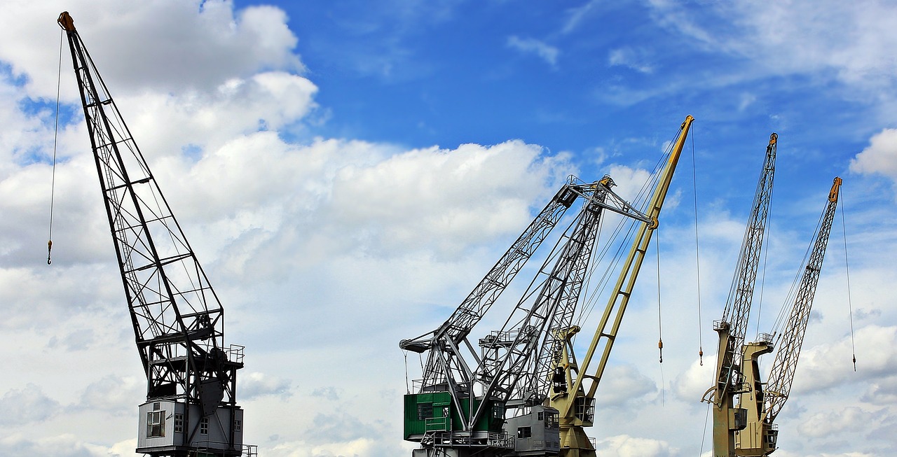 a group of cranes sitting on top of a body of water, a photo, pixabay, figuration libre, under blue clouds, mechanical superstructure, view from the side”, photostock