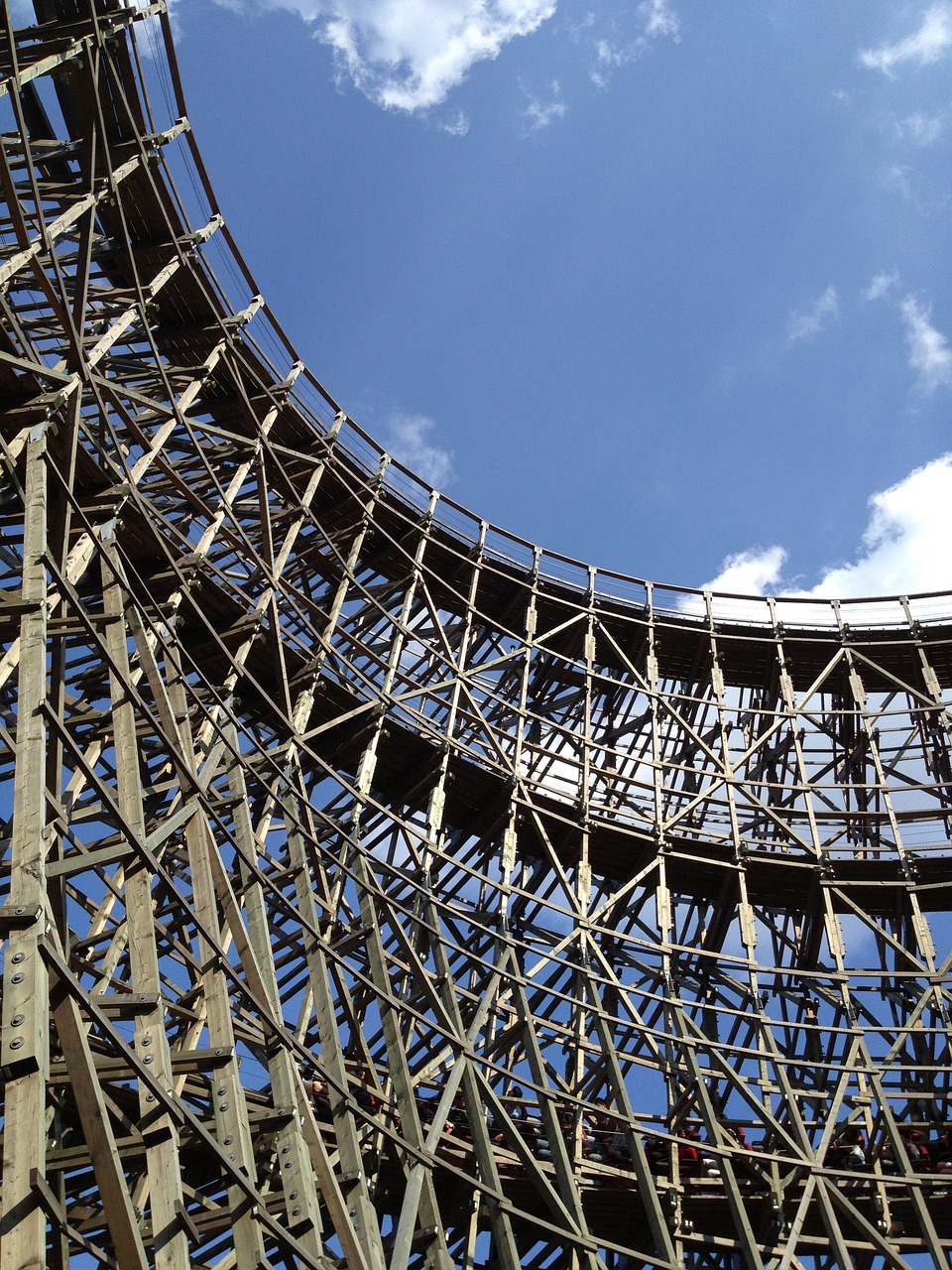 a wooden roller coaster against a blue sky, by Edward Corbett, flickr, extreme intricate metal details, in tokio, show from below, in the sun