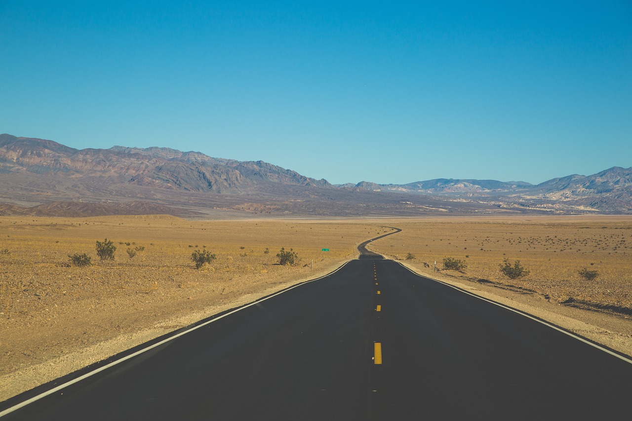 a road in the middle of a desert with mountains in the background, a picture, by Whitney Sherman, shutterstock, postminimalism, analog photo, tyler west, completely empty, savannah