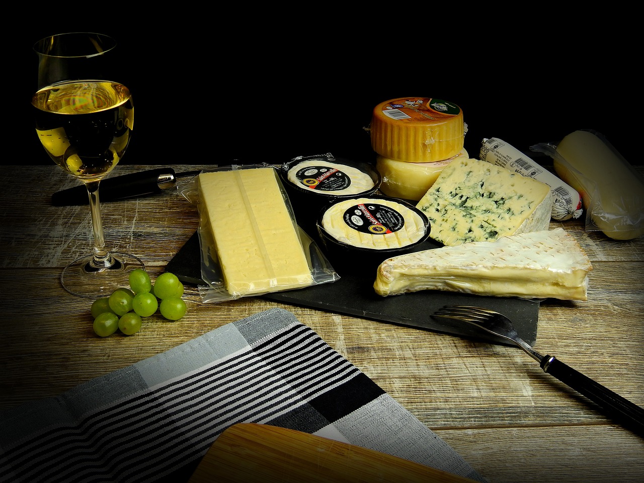 a table topped with cheese and grapes next to a glass of wine, a still life, by John Wilson, pexels, dau-al-set, on black background, advert, on a sunny day, cheeses