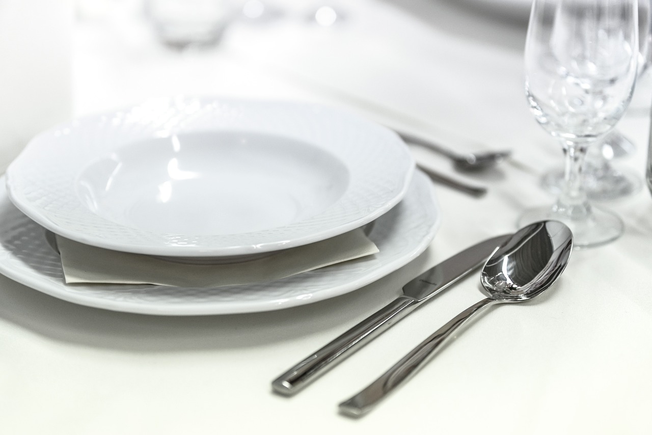 a white table topped with plates and silverware, by Adam Marczyński, istock, steel plating, close - up photo, villany