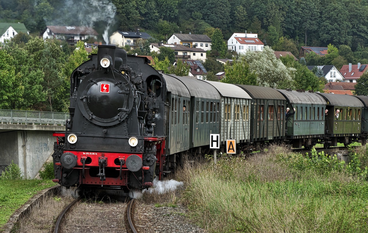 a train traveling down train tracks next to a lush green hillside, a picture, by Jörg Immendorff, pixabay, set in ww2 germany, steam trains, zdislav beksinsk - h768, festivals