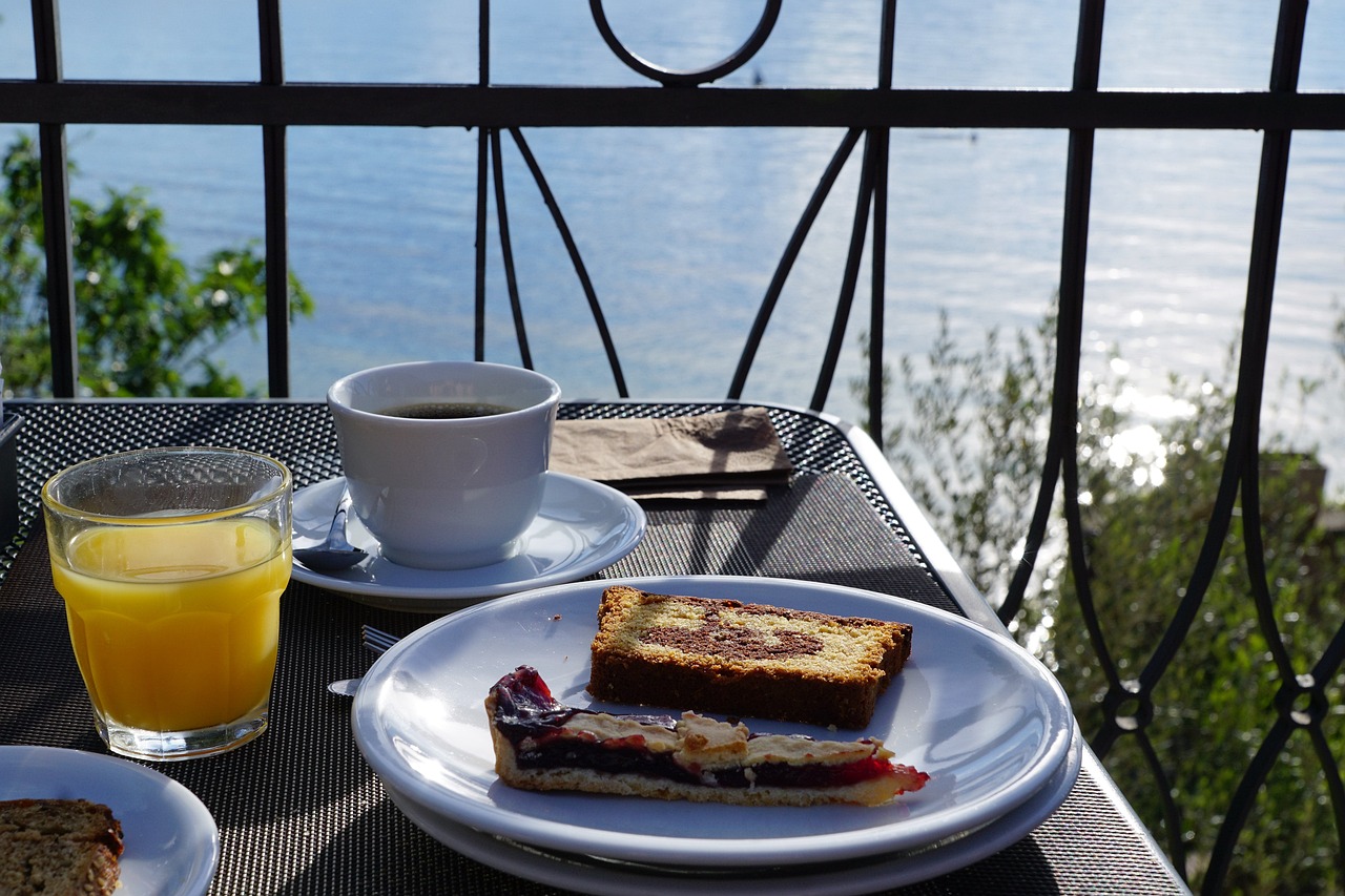a table topped with plates of food next to a glass of orange juice, by Dietmar Damerau, pexels, art nouveau, lake view, brown bread with sliced salo, coffee, cuban setting
