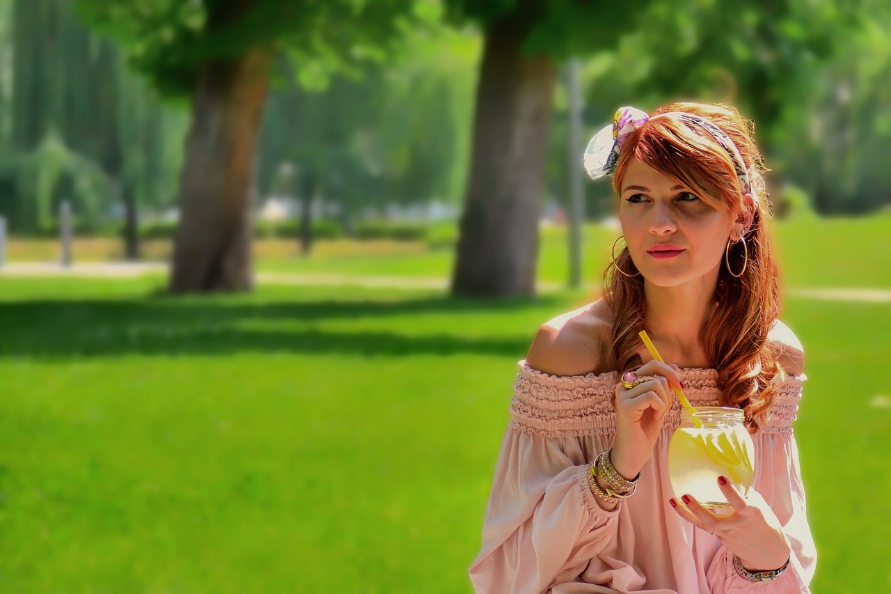 a woman standing in a park holding a drink, by Igor Grabar, trending on pixabay, renaissance, pink and yellow, cute young redhead girl, widescreen, hot summertime hippie