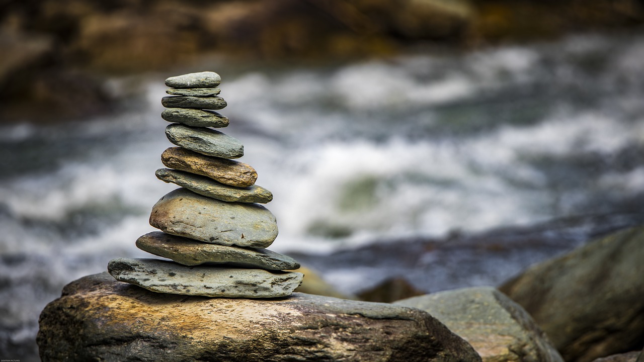 a stack of rocks sitting on top of a rock next to a river, a tilt shift photo, mid shot photo