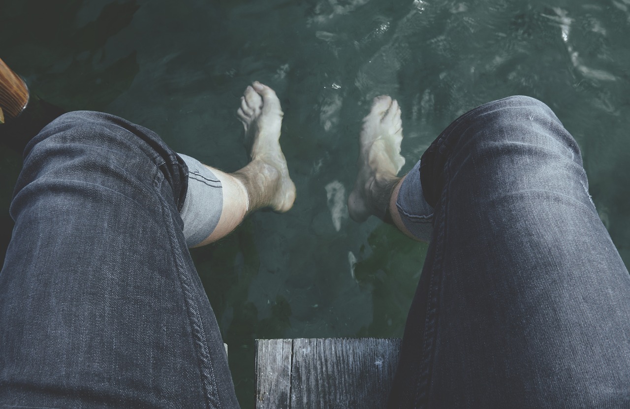a person standing on a dock next to a body of water, pexels, realism, detailed shot legs-up, sitting on man's fingertip, floating. greenish blue, ( ( ( wearing jeans ) ) )