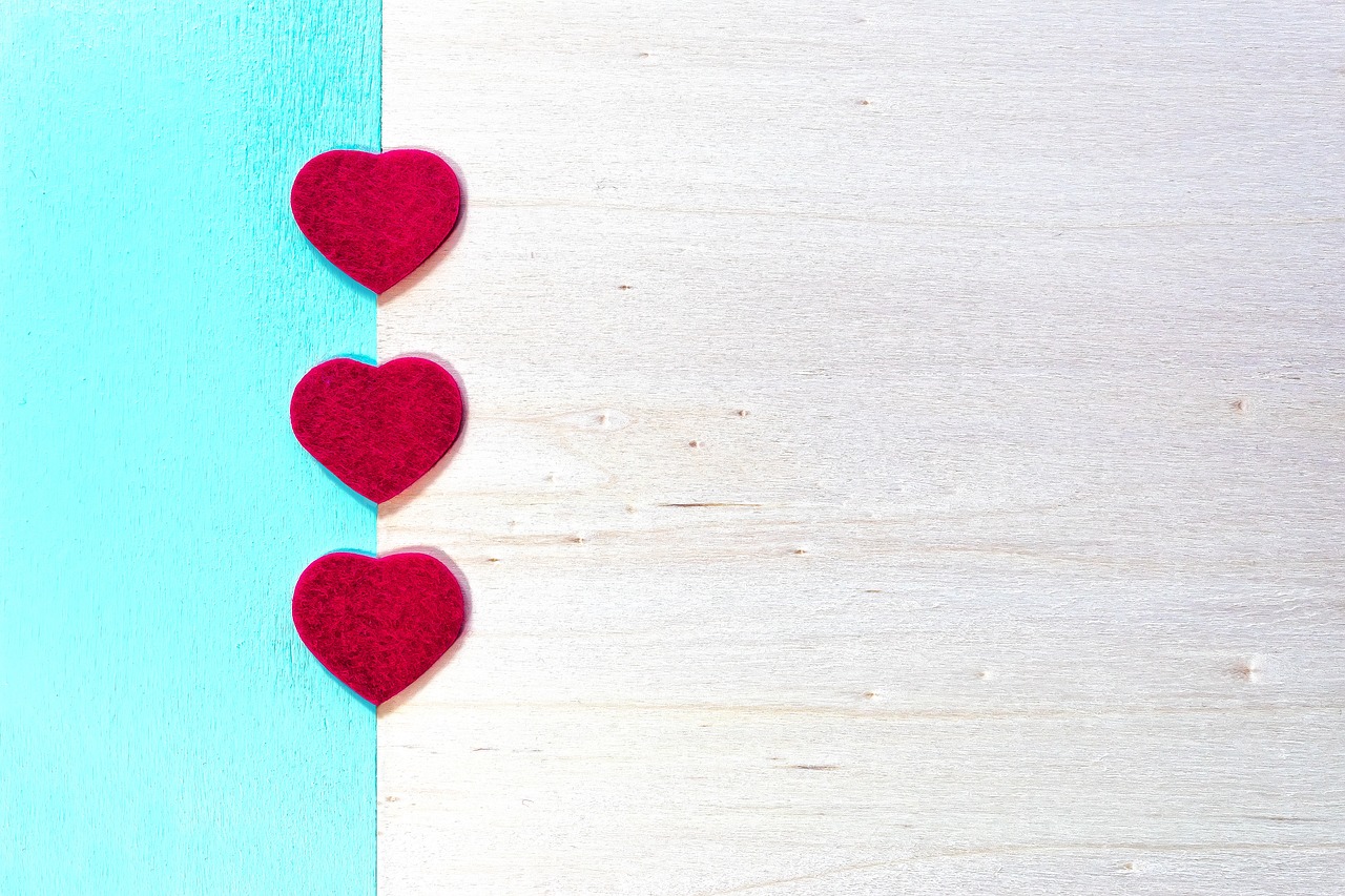 a couple of red hearts sitting on top of a blue and white wall, a stock photo, minimalism, made of wood, turquoise color scheme, three fourths view, layed on a red velvet fabric