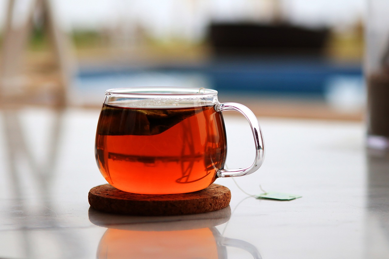 a cup of tea sitting on top of a wooden coaster, pexels, glassy, wikimedia commons, honey, botanicals