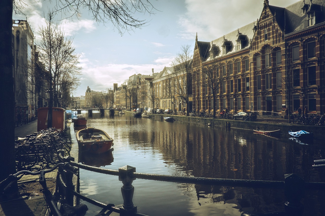 a canal filled with lots of boats next to tall buildings, a picture, by Jacob Toorenvliet, pexels contest winner, happening, ( rembrandt ), retro effect, college, parliament