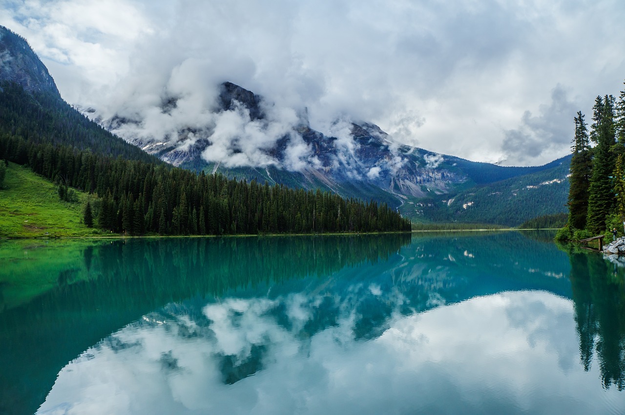 a body of water with a mountain in the background, a picture, by Raymond Normand, shutterstock, overcast lake, teals, high definition 4 k photo, build in a forest near of a lake