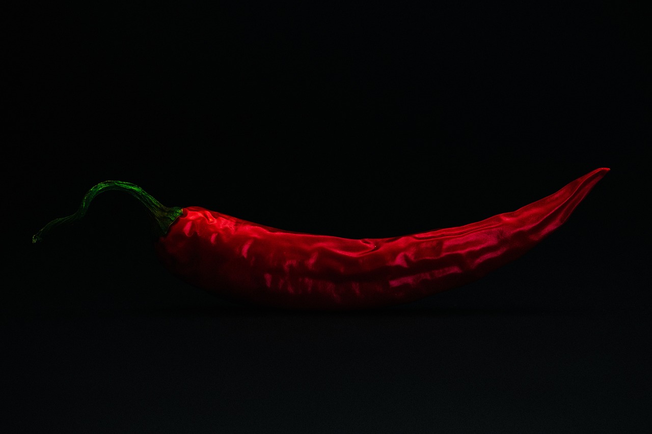 a red chili sitting on top of a black surface, a picture, by Jan Rustem, pexels, hyperrealism, lit from the side, really long, background image, cloth simulation with houdini