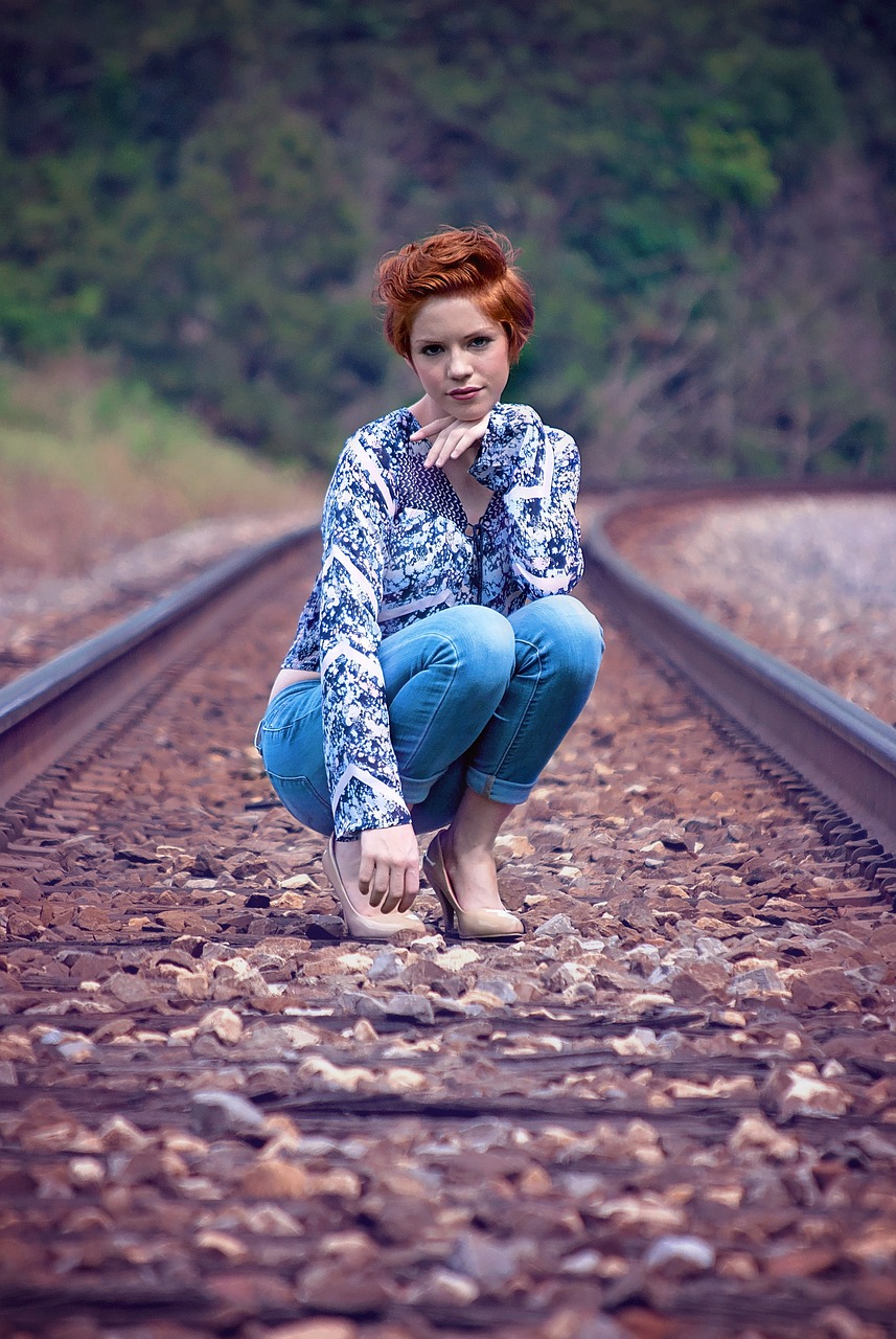 a woman crouching down on a train track, a portrait, by Galen Dara, flickr, beautiful redhead woman, batik, blue clothing, full length photo