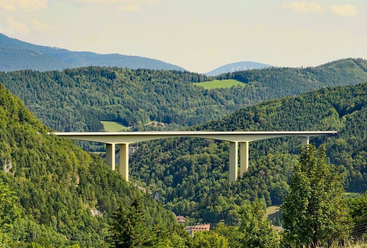 a large bridge over a lush green hillside, a picture, by Werner Gutzeit, shutterstock, overlooking a vast serene forest, concrete, detailed zoom photo, integrated in the mountains