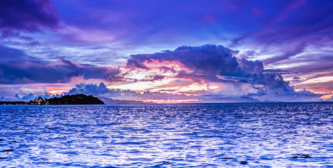 a large body of water under a cloudy sky, inspired by Edwin Georgi, shutterstock, at purple sunset, island in a blue sea, vibrant and vivid color, enhanced photo
